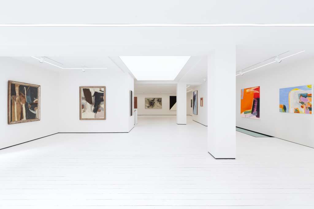 Modern gallery space with white walls, skylights, and contemporary artwork displayed on walls.