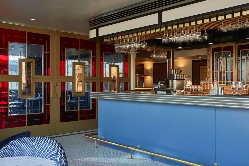 Bar and restaurant interior with blue counter, hanging glassware, red entry doors, and modern lighting fixtures.