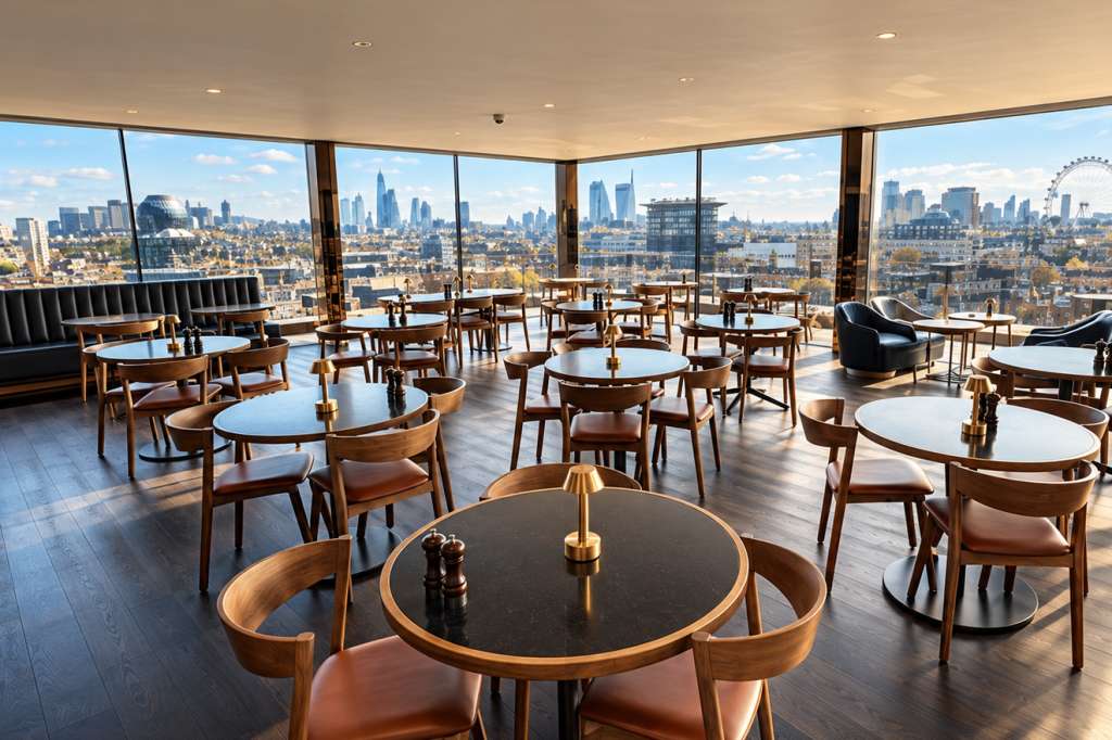 Rooftop bar and restaurant with round tables, mid-century chairs, and panoramic city skyline views through floor-to-ceiling windows.